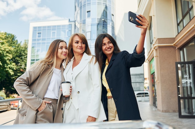 Using phone Women in formal wear is outdoors in the city together