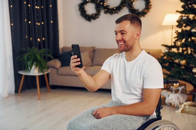 Using smartphone to communicate with people New year is coming Disabled man in wheelchair is at home