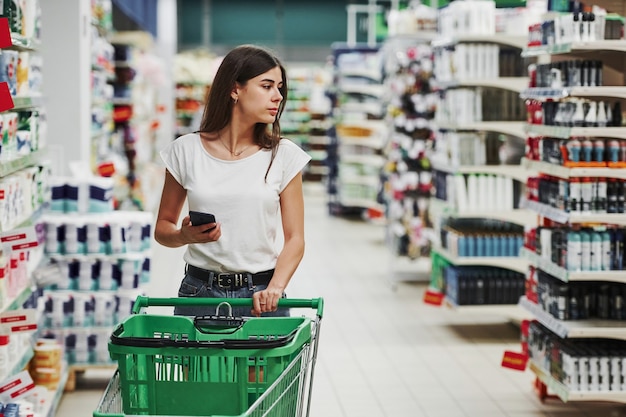 Using smartphone. Female shopper in casual clothes in market looking for products.