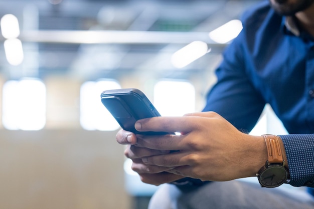 Photo using smartphone man in blue shirt checking messages in modern office