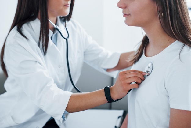 Using stethoscope Young woman have a visit with female doctor in modern clinic