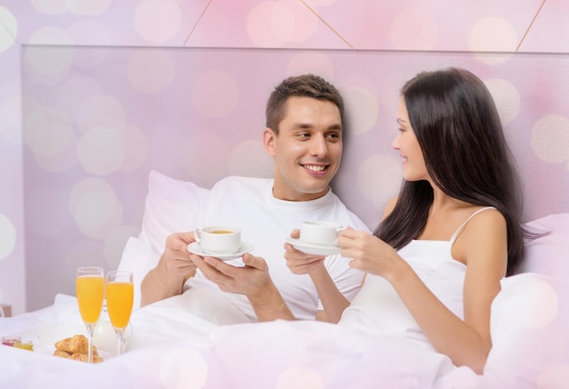 vacation, holidays, people, romance and valentines day concept - happy couple having breakfast in bed at hotel or home over lights background