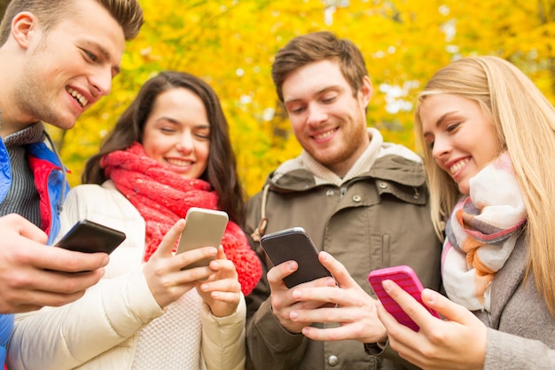 vacation, people, technology and friendship concept - group of smiling friends with smartphones in autumn park