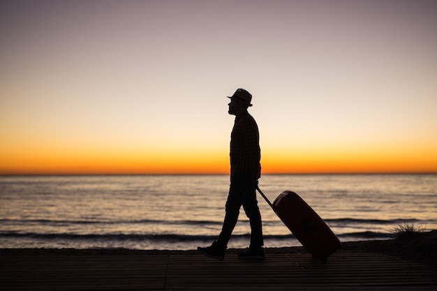 Photo vacation summer and travel concept  young man silhouette with suitcase at sunset near the sea