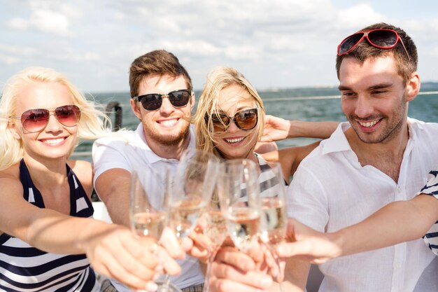 vacation, travel, sea, friendship and people concept - smiling friends with glasses of champagne on yacht