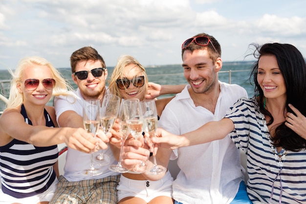 vacation, travel, sea, friendship and people concept - smiling friends with glasses of champagne on yacht