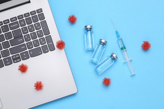 Photo vaccination covid 19 treatment laptop and vaccine bottles with blank label for brand virus molecules and syringe on blue background top view flat lay