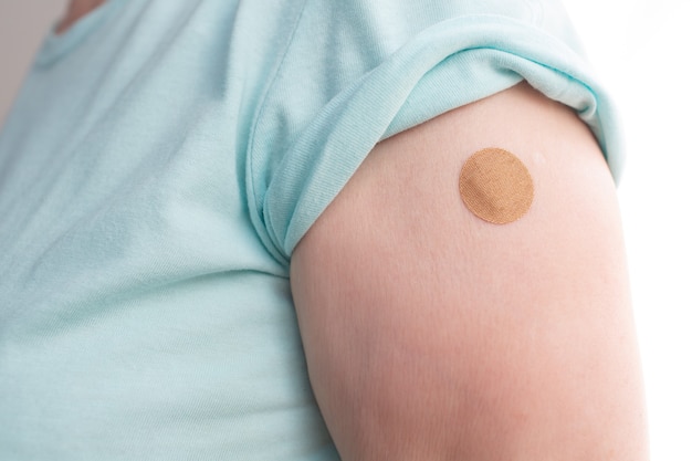 Photo vaccination elderly woman in doctor office with adhesive covid-19 vaccine plaster.