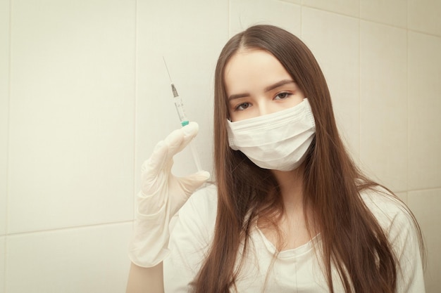 Vaccinations and vaccines Girl in a medical mask with a syringe in her hands in a hospital