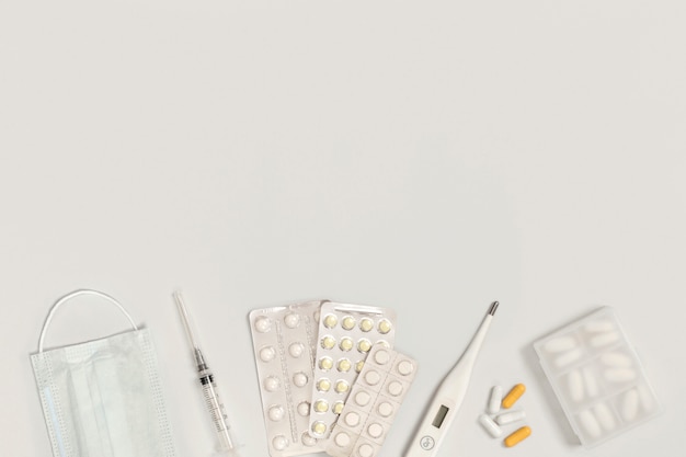 Vaccine, protective medical mask, pills, syringe, thermometer, tablet holder on a white background with space for text. Treatment of colds and flu.