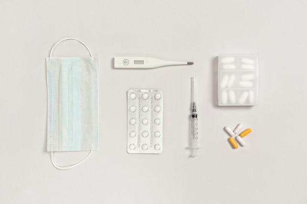 Vaccine, protective medical mask, pills, syringe, thermometer, tablet holder on a white background with space for text. Treatment of colds and flu.