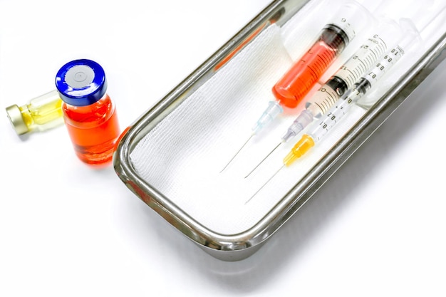 Vaccine in vials and plastic syringes with medical needles put in a medical stainless steel container for ready injection to patient on white background