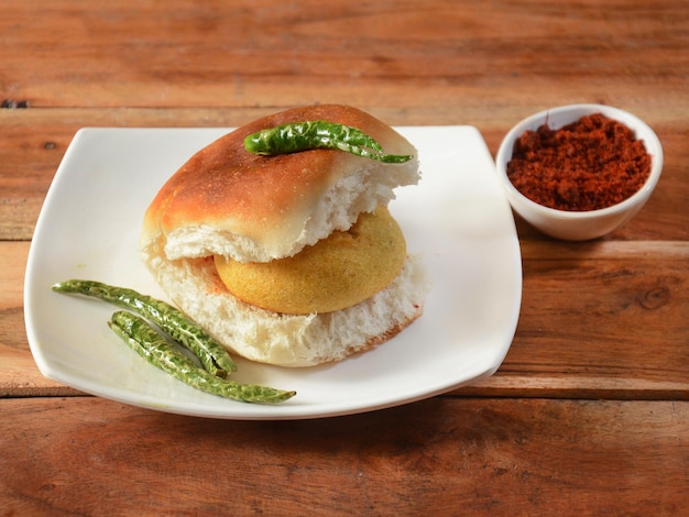 Vada Pav Mumbai Famous vada paav is an indian burger Potato patty is deep fried and stuffed inside a paav or bun like burger served over a rustic wooden background selective focus