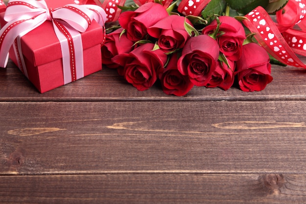 Valentine background of gift box and red roses on wood. Space for copy.