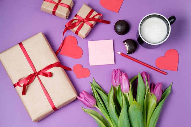 Photo valentine background with gift box sweet hearts and tulips on violet table top view flat lay