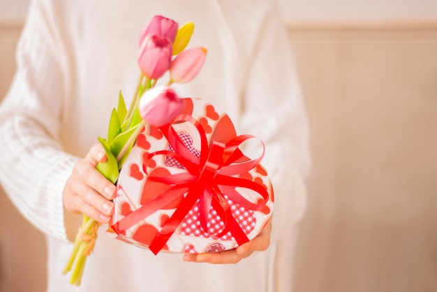 Valentine Day cardarms holding gift box with heart shaped bowand flowesHand give gift with flowers