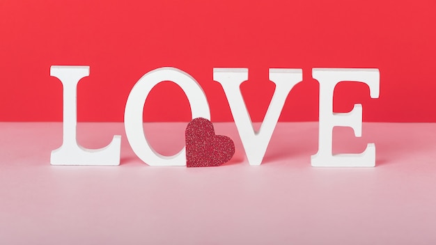 Valentine day concept with white love letters and a red heart on pink and red background