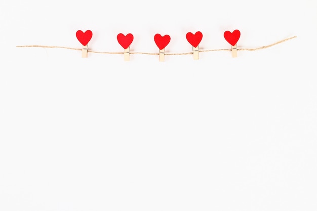 Valentine day layout. Red hearts on wooden clothespins on a jute twine on a white background.