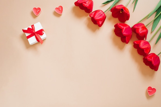 Valentine Day Romantic Background. Red tulips, a gift with a bow, and candle hearts on a beige background with copying space. Flat lay