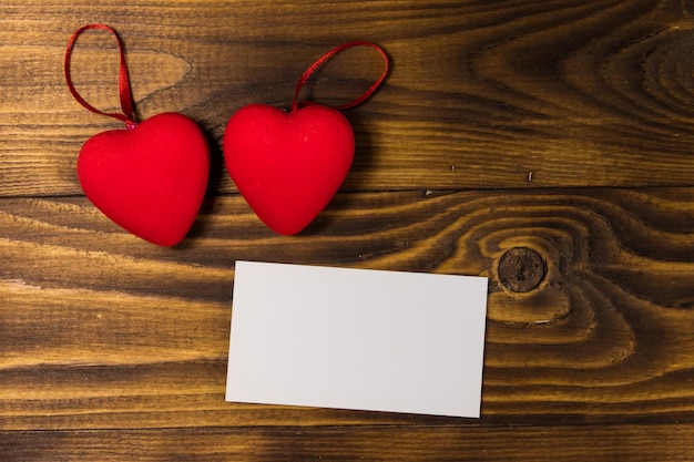 Valentine's day blank greeting card and two red hearts on wooden background. Top view, copy space