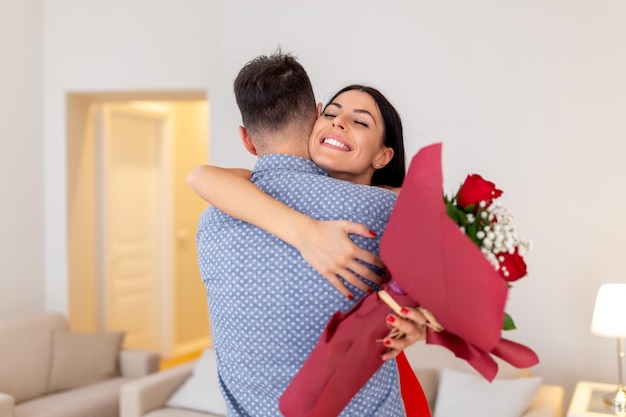 Valentine's Day concept Happy couple in love with A young loving couple celebrating Valentine's Day Lovers hugging each other Handsome man surprises his girlfriend with red roses at home