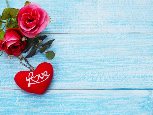 Valentine's day greeting card background with copy space. Red roses and key chain red heart shape with word love on blue wooden table.