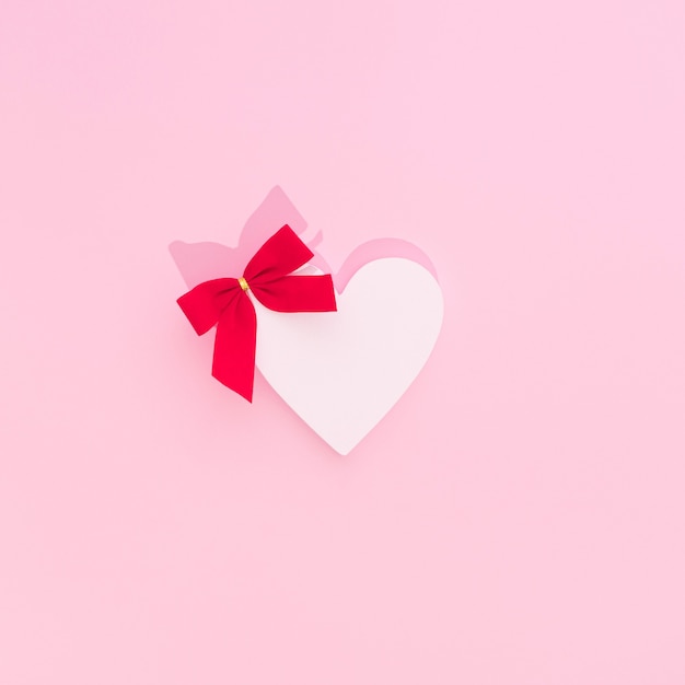 Valentine's heart with a bright red bow on soft pink background. Minimal flat lay composition.