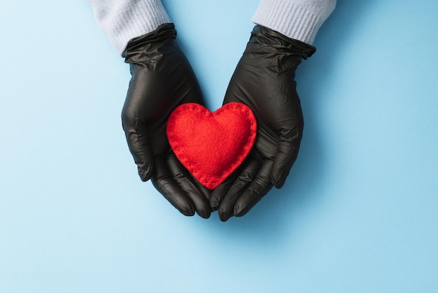 Valentines Day in 2021 during the Covid-19 pandemic and coronavirus disease. Red heart on the palms of a woman protected by medical gloves