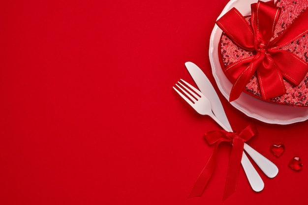 Valentines day background or concept with empty pink plate and whiteware on scarlet or red background. Top view flat lay with copy space.