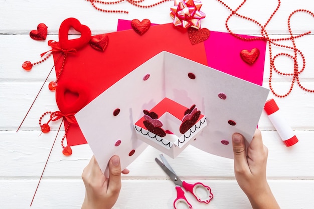 Valentines day background. Handmade gift greeting card creating, cut and paste, craft paper, felt and diy tools on white wood. Above view, flat lay