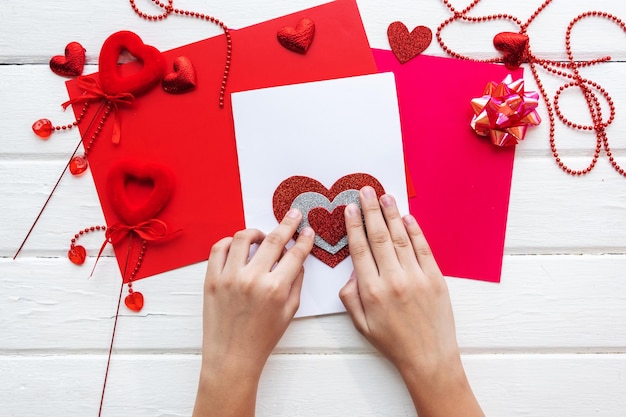 Valentines day background. Handmade gift greeting card creating, cut and paste, craft paper, felt and diy tools on white wood. Above view, flat lay