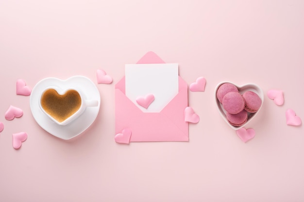 Valentines Day card. Pink empty envelope with blank white note mockup inside, macaron macaroon cookie and heart shaped coffee cup on pink background. 8 March, Valentines Day, Birthday card. Mock up.