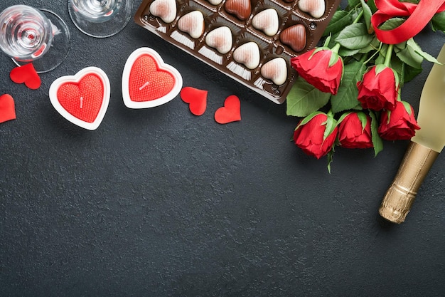 Valentines day card Rose red flowers brownie cookies and chocolate candy on heart shaped gift box with wine on black background Mothers or Womens Day greeting card Top view flat lay