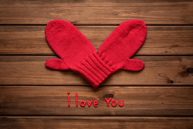 Valentines day card with heart made of red mittens on wooden vintage background and phrase about love