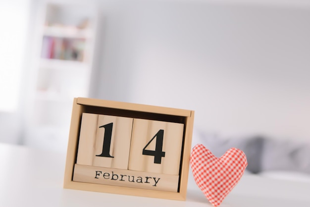 Valentines day concept Hand make yarn red heart beside wooden block calendar set on Valentines date 14 February on table and bright room background Happy valentine day