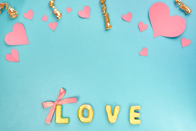 Valentines day concept Pink paper hearts confetti and word love on blue background Top view