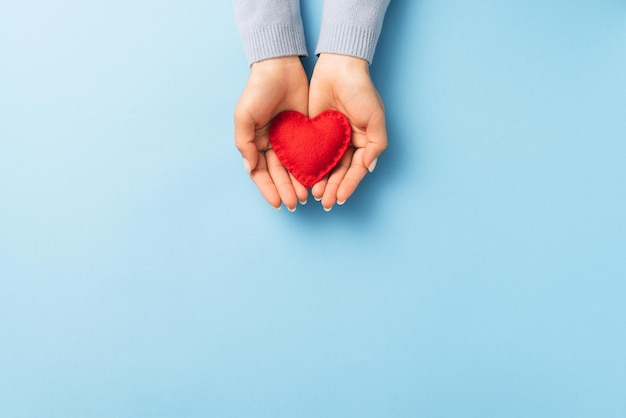 Valentines day concept with a red heart in a handful of a woman on a blue background with copy space