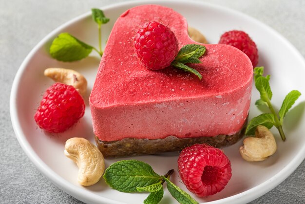 Valentines day dessert. heart shaped raw vegan red cake with raspberries and mint in a plate. healthy delicious food