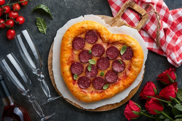 Valentines day heart shaped pizza with mozzarella pepperoni and basil wine bottle two wineglass gift box on black background Idea for romantic dinner Valentines day Top view Mock up