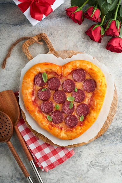 Valentines day heart shaped pizza with mozzarella pepperoni and basil wine bottle two wineglass gift box on light grey background Idea for romantic dinner Valentines day Top view Mock up