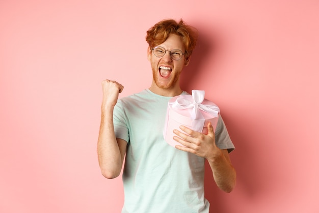 Valentines day and romance concept cheerful redhead guy making fist pump and scream yes with joy hol...