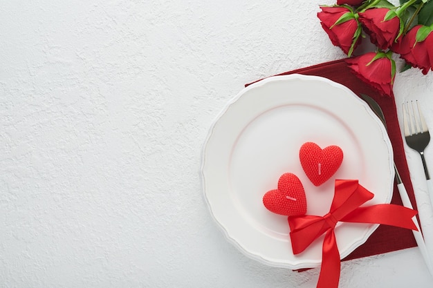 Valentines day romantic table setting Empty or closeup of a dinner black plate knife fork and decorative silk hearts on white background Holiday concept Copy space for inscriptions