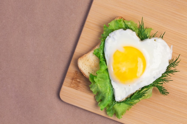 Valentines day sandwich made from fried bread, fried egg in the shape of a heart and a leaf of lettuce