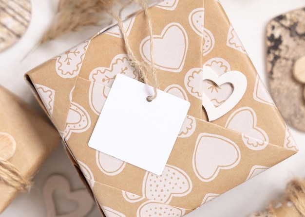 Valentines kraft paper wrapped present with square gift tag and hearts close up Spring scene with blank label Rustic cottage chic or bohemian mockup copy space