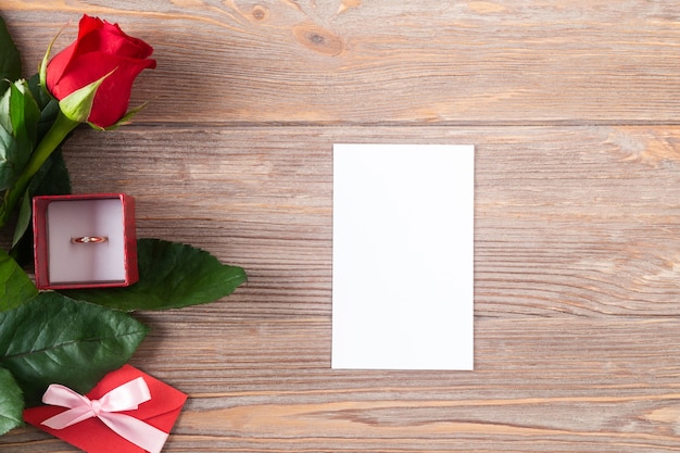 Valentines mockup with red rose and golden ring on the wooden background, flat lay with copy space, white card.