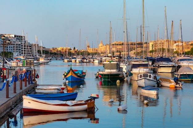 Valletta harbour with yachts and multicolored fishing boats Luzzu with eyes, church and fortress, illuminated by sunset light, Malta