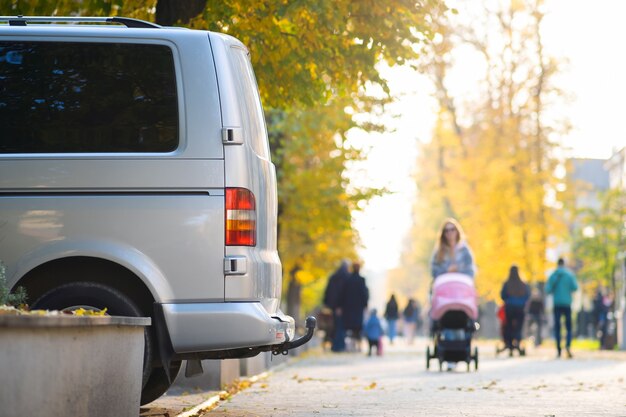 Van parked on a city street side on bright autumn day with blurred people walking on pedestrian zone.