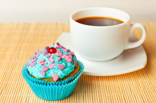 Vanilla cupcake with whipped cream and red currants and colored sprinkles with a cup of coffee.