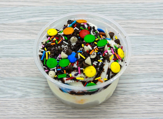 Vanilla ice cream topping with vanilla chips chocolate chips sprinkles and bunties served in disposable cup side view of indian and pakistani dessert