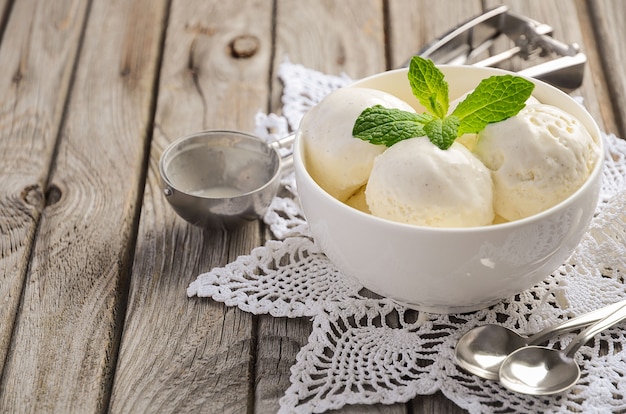 Vanilla ice cream with mint leaves in white bowl on rustic wooden table.